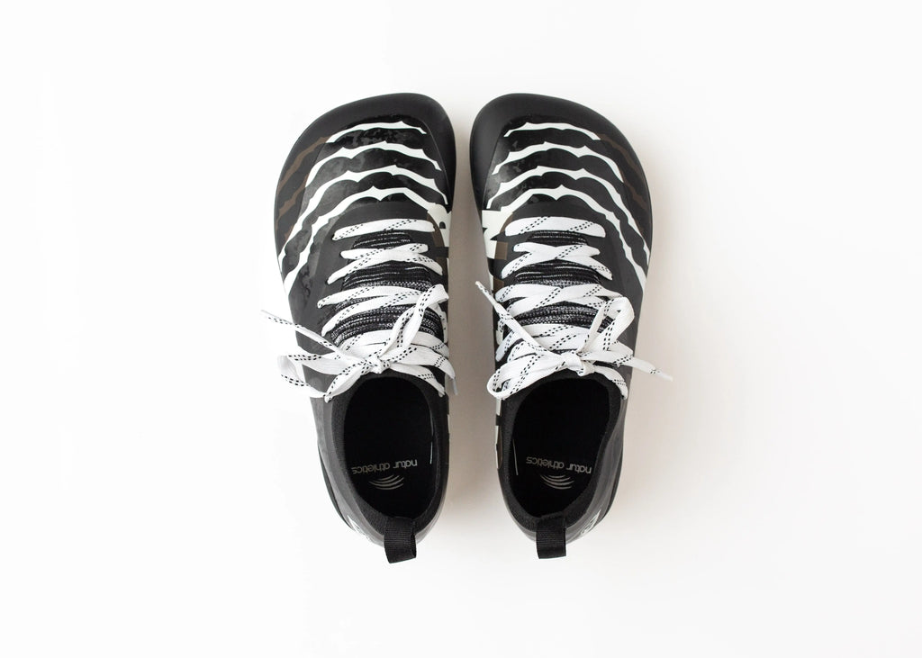 Close-up shot of Natur Athletics adult minimalist barefoot cleat's wide toe box and sleek black design, demonstrating its natural fit. The cleat features a patented cleat plate system for enhanced performance, offering dynamic flexibility and superior traction for athletes
